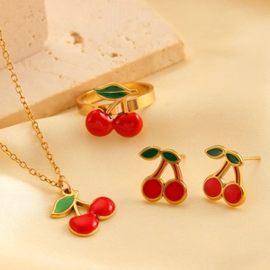 Détail d'une parure de bijoux cerise dorée avec fruits rouges sur soie et pierre texturée