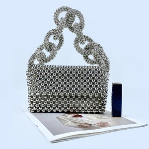 Detail view of a silver beaded evening bag with interlocking ring handles on blue surface