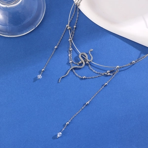 Detail van zilveren gelaagde ketting met slangenhanger en kralenfranje op blauw vlak