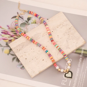 Colorful clay bead necklace with faux pearls and black heart pendant on beige stone base