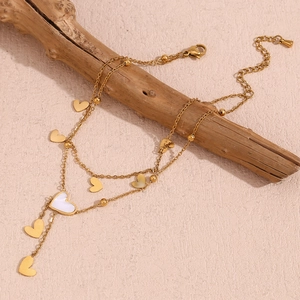 Double-layered 18K gold-plated heart anklet with white shell tassel on a wooden branch