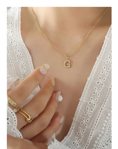 Detailed view of a gold-plated necklace with a zircon-inlaid letter G pendant on a model