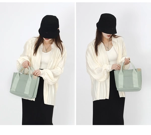 Detail view of light green canvas tote bag showing the side leather tag and fabric texture