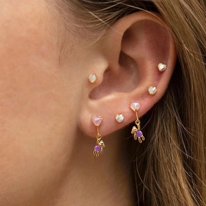 Macro shot of gold heart studs and purple beaded bear drop earrings on model