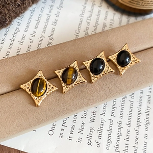 Close-up of vintage tiger eye and black stone star earrings on a velvet display stand