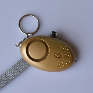 Detail of golden personal security alarm with LED light, loud speaker, and keychain