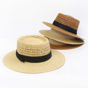 Detailed stack of woven straw boater hats in beige and tan with black silk ribbons