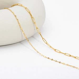 Close-up of gold paperclip and shimmering curb chain necklaces on white background