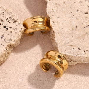 Gros plan de boucles d'oreilles concaves dorées à l'or 18 carats sur pierre beige