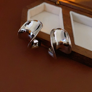 Close-up of C-shaped silver metal hoop earrings with a polished finish on a wooden box