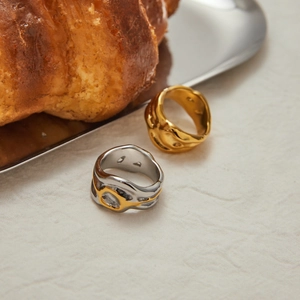 Modern lava-style gold and silver-toned stainless steel rings on a white fabric background