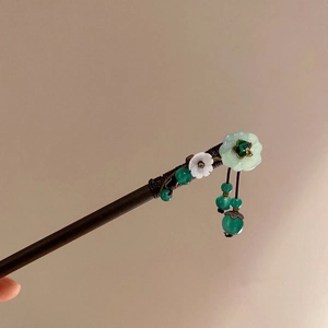 Détail d'un pic à cheveux en bois vintage avec pétales de jade et gland de Pipa