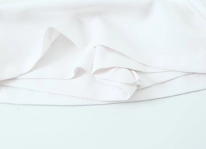 Close-up detail of the white fabric texture and hemline on a stylish skort with belt
