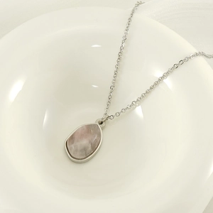 Detail of pink natural stone pendant on 18k gold plated chain in white ceramic tray