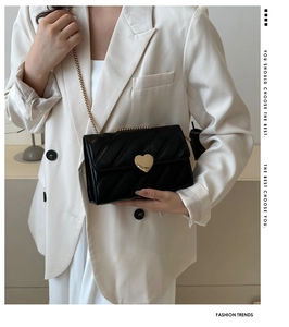 Detail of black quilted crossbody bag featuring golden heart-shaped lock and chain strap