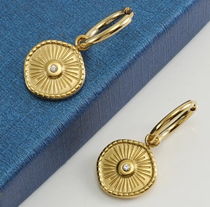 Close-up of golden 18K steel hoop earrings with sunburst pattern and central crystal