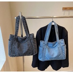 Detail view of denim tote bags in dark grey and light blue hanging on a metal rack