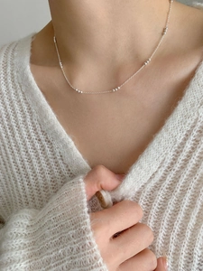 Close-up of minimalist sterling silver bead chain necklace worn on a neck over a white sweater