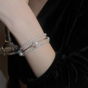 Dettaglio di un set di bracciali a più strati con strass e perle indossato al polso