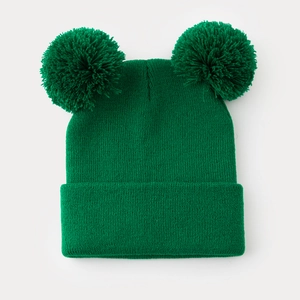 Dettaglio del berretto in maglia verde con due pompon che mostra la trama del punto