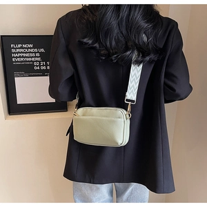 Detail of light green PU camera bag with patterned wide strap worn over a black blazer