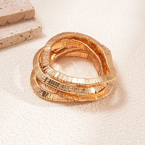 Macro detail of stacked gold geometric metal bangles with wave texture and modern design