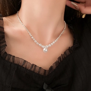 Detailaufnahme einer künstlichen Perlenkette mit Anhänger am Hals eines Modells