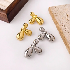 Minimalist gold and silver bow stud earrings displayed with wooden jewelry box and stones