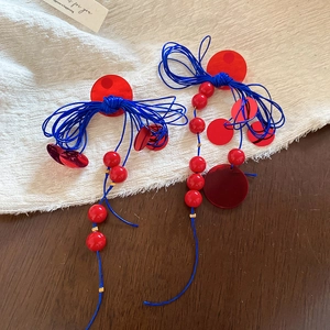 Detail of ethnic style resin earrings with red and blue beads, weaving, and tassel fringe