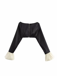 Detail eines schwarzen Crop-Tops mit silbernem Reißverschluss und weißen Rüschenmanschetten