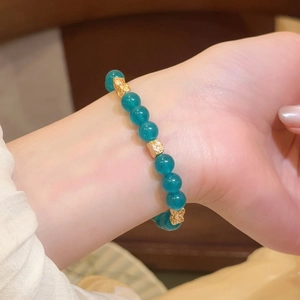 Primer plano de una pulsera de cuentas de piedra natural verde azulado con dijes dorados en la muñeca.