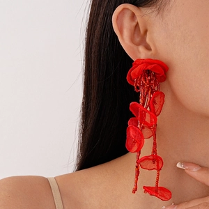 Close-up of red woven petal earrings with beaded tassels worn by a model