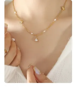 Detail of gold star and pearl chain necklace with a triangular zircon pendant on model