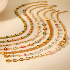 Detailaufnahme goldener Edelstahlarmbänder mit bunten Emaille-Blumen und Perlen
