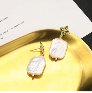 Close-up of baroque pearl earring with golden flower and green gemstone on metal tray