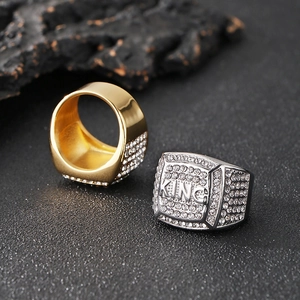 Hip hop style gold and silver plated KING rings with cubic zirconia on stone background