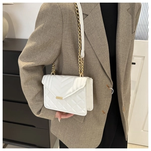 Détail d'un sac matelassé blanc avec chaîne dorée porté sur un blazer marron élégant