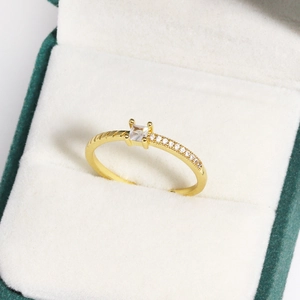 Detailaufnahme eines vergoldeten Rings mit eckigem Zirkonia in einer grünen Samtbox