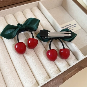 Detail of satin bow hair clips with glossy red cherries on a beige jewelry box