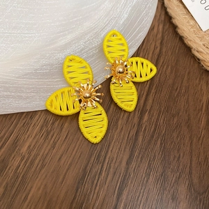 Detailed view of woven yellow flower earrings with gold center on a rustic wooden surface
