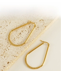 Détail macro des boucles d'oreilles goutte d'eau dorées avec finition gaufrée