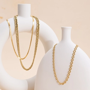 Three gold stainless steel layered snake and cuban necklaces on white ceramic decor