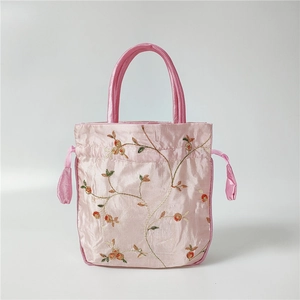 Detail of pink satin handbag with golden floral embroidery and drawstring closure