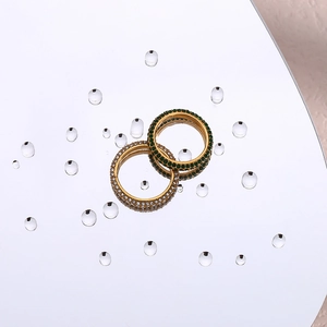 Detailed close-up of two gold rings with full-circle green and white zircon stones on water surface