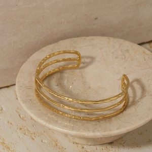 Minimalist gold three-layer open bangle with a handcrafted hammered texture on marble