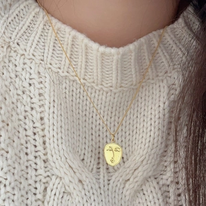 Detail of a minimalist gold-plated oval face pendant necklace worn over a white sweater