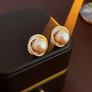 Macro view of gold pearl earrings with zircon stones on black leather jewelry box