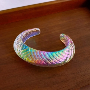 Macro detail of iridescent glass open bangle with spiral texture on wood base