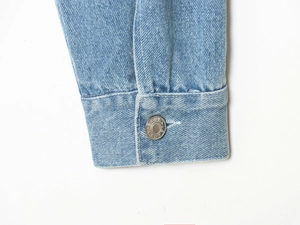 Nahaufnahme der hellblauen Jeansmanschette mit Silberknopf und feiner Textur