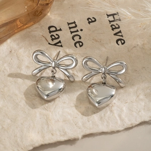 Detail shot of silver bow heart earrings on a stylized paper background with soft lighting
